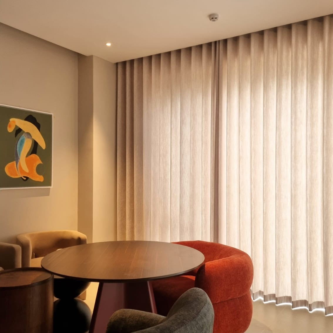 Floor-to-ceiling ripple fold drapes in the Lune collection, unlined, in warm sand — installed ceiling height in a modern lounge setting with light filtering softly through the fabric