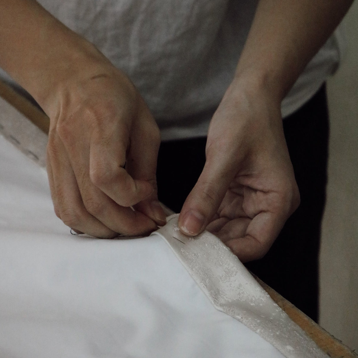 Artisan hands pinning and setting pleats on a white linen drapery panel during the hand-finishing process at Thoa Home's workshop.